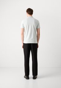 Světle modrá polo tričko s krátkým rukávem a minimální texturou, nahoře s černými kalhotami a tmavými botami, viděné zezadu.