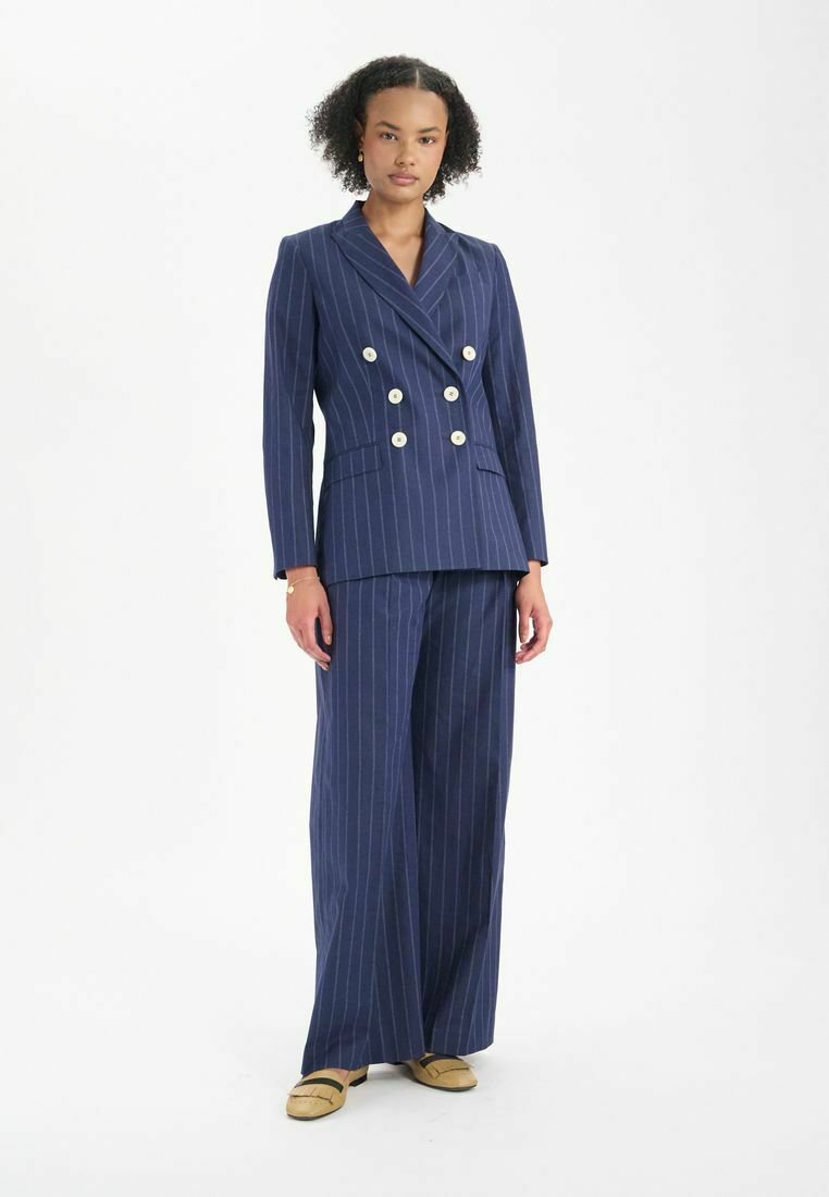 Blazer marine à rayures à double boutonnage avec boutons dorés, associé à un pantalon large. Tissu lisse avec une coupe ajustée.