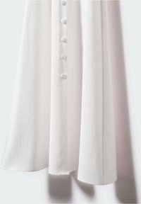 Valkoinen mekko, jossa on pehmeästi laskeutuva kangas, viiden napin etuläppä ja kaareva helma.
