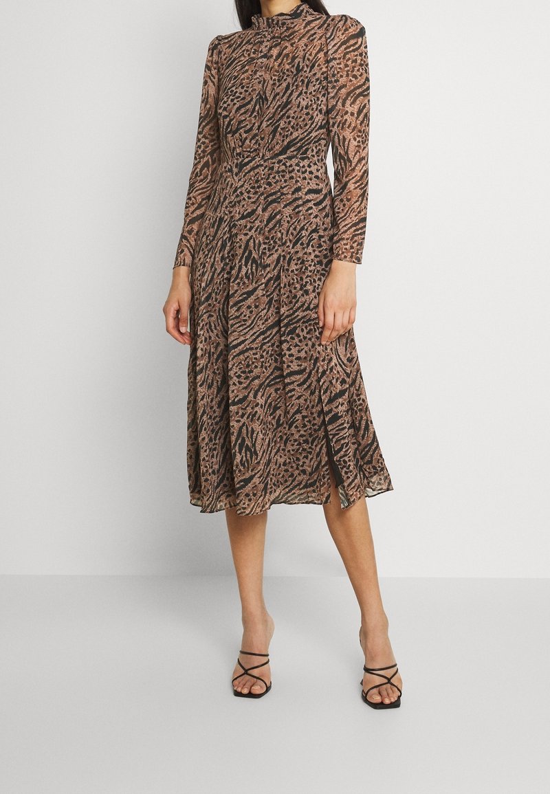 Langärmliges, plissiertes Midikleid aus einem durchsichtigen, braunen Tierdruckstoff mit hohem Kragen und seitlichen Schlitzen. Kombiniert mit schwarzen Riemchensandalen.