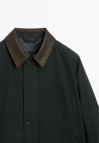 Dark green jacket with a brown leather collar, snap button closure, and side pockets. Made from matte fabric with a textured finish.
