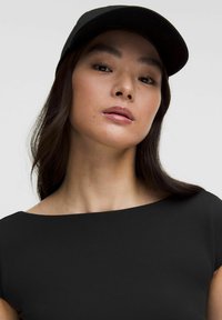 Casquette noire avec une visière incurvée, portée avec un simple top noir à encolure large. Texture lisse et design ajusté.