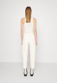 Biały dopasowany top na ramiączkach w połączeniu z białymi, wysokim stanem spodniami. Widok z tyłu, gładka faktura, styl minimalistyczny, kontrastujące botki do kostek.