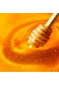 Złoty miód o gładkiej teksturze, wirujący w płynnej formie, z drewnianym maczadełkiem z rowkami zanurzonym i błyszczącymi bąbelkami.