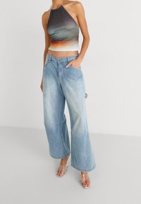 Crop top s halter krkem s gradientem od tmavě šedé k oranžové, v kombinaci se světle modrými širokými džínami. Průhledné sandály na podpatku.