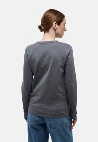 Chemise grise à manches longues avec col rond et coupe décontractée, fabriquée en matériau doux. Coutures visibles et texture subtile.