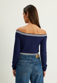 Marinblå off-shoulder tröja med vita ränder, ribbade Ärmar och nederkant, kombinerad med blå denim jeans med hög midja och bakfickor.