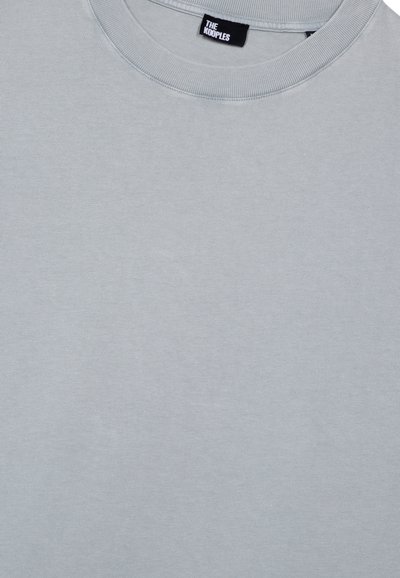 Camiseta de algodón gris claro con un cuello redondo ribeteado. Presenta una pequeña etiqueta con "THE HOOPLES" en el interior del cuello. Textura suave.