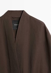 Bruine linnen kimono-stijl jas met brede kraag en zichtbaar merkembleem aan de binnenkant van de halslijn.