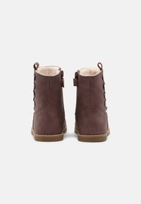 Bottes chelsea en cuir brun avec une doublure en polaire douce, présentant un extérieur lisse, un bout arrondi et des boutons décoratifs sur le côté.