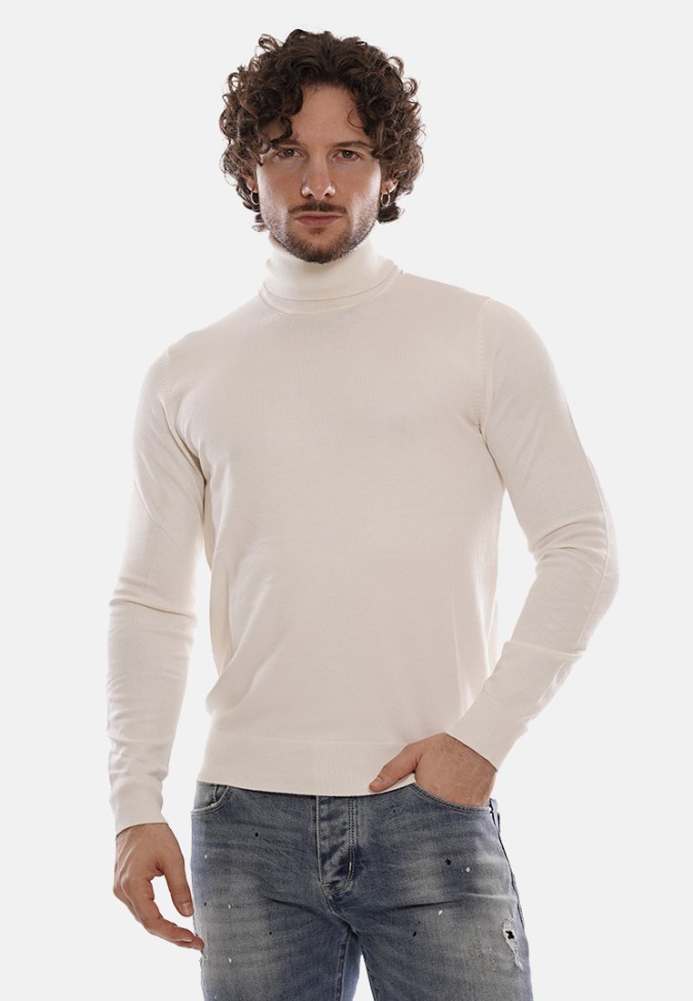 Maglione a collo alto color crema con design attillato, realizzato in tessuto morbido con polsini e orlo a costine. Indossato con jeans blu strappati.