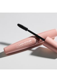 Rosa Mascara-Röhre mit abgerundetem Design, ausgestattet mit einem schwarzen Bürsten-Applikator. Der Text lautet "The Lash Styler Volume Mascara" in Weiß.