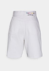 Valkoiset farkkushortsit, joissa on hapsureuna, kaksi takataskua ja monivärinen "Tämä on rakkautta" -etiketti vyötärönauhassa.