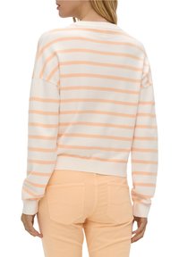 Gestreifter Pullover in Weiß und sanften Apricottönen, mit einer lockeren Passform, gerippten Bündchen und einem cropped Design. Getragen mit hellen Apricot-Hosen.