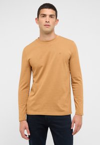 Langarmshirt mit Rundhalsausschnitt aus senffarbenem Stoff, mit schmaler Passform und kleinem gesticktem Logo auf der Brust. Glatte Textur, minimalistisches Design.