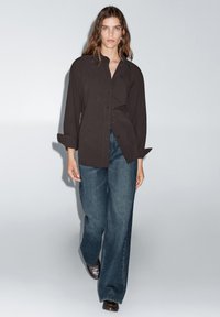 Sort skjorte med knapper i afslappet pasform og unik fald, parret med højtaljede, brede mørke denim jeans og brune flade sko.