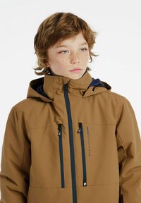 Braune wasserfeste Jacke mit hohem Kragen, marineblauen Akzenten und mehreren Reißverschlusstaschen. Das Material hat eine glatte Textur und ist für den Außenbereich konzipiert.
