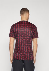 Lyhythihainen urheilupaita mustassa ja punaisessa geometrisella kuviolla. Valmistettu sileästä, kevyestä kankaasta, jossa on pyöreä pääntie.