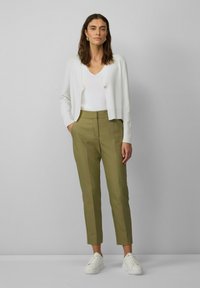 Witte, knop-up cardigan over een witte v-hals top, gecombineerd met olijfgroene, op maat gemaakte broek en witte sneakers. Gladde texturen en een aansluitend ontwerp.