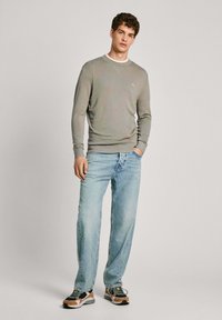 Pull gris avec un col rond et des poignets côtelés, associé à un jean bleu clair et des baskets multicolores. Look décontracté.