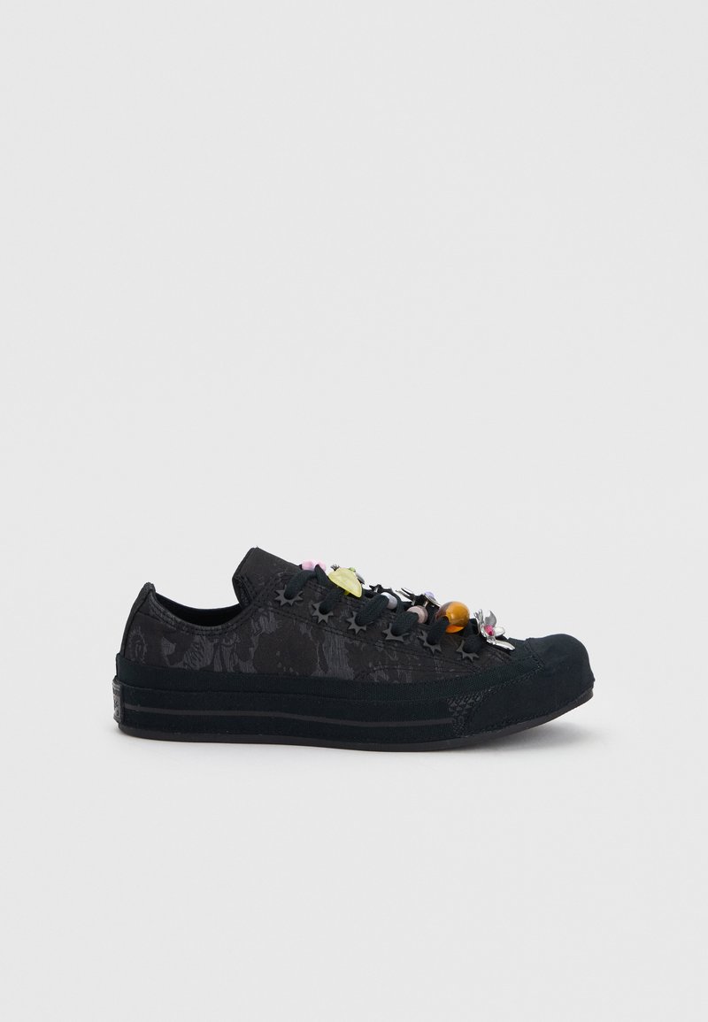 Black low-top sneaker with floral pattern and colorful decorative charms attached to the laces on a plain background.