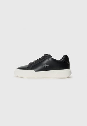 Baskets en cuir noir avec semelles en caoutchouc blanc, présentant un bout rond, un laçage avant et des détails de logo sur les côtés pour l'identité de marque.
