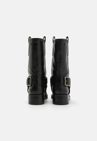 Botines de cuero negro presentan una punta redondeada, un tacón robusto y hebillas decorativas, con detalles de costuras y lengüetas en los laterales.