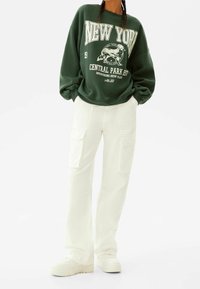 Zelená mikina s grafikou "NEW YORK CENTRAL PARK", v kombinaci s bílými cargo kalhotami s bočními kapsami a rovnými nohavicemi.