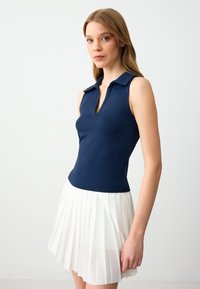 Polo top senza maniche di color navy con colletto, abbinato a una gonna plissettata bianca, che mette in risalto texture lisce e linee definite.