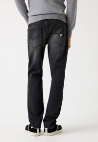 Jeans negri din denim cu o croială dreaptă, ce au două buzunare la spate și un mic logo pe buzunarul din dreapta. Purtați cu adidași negri.