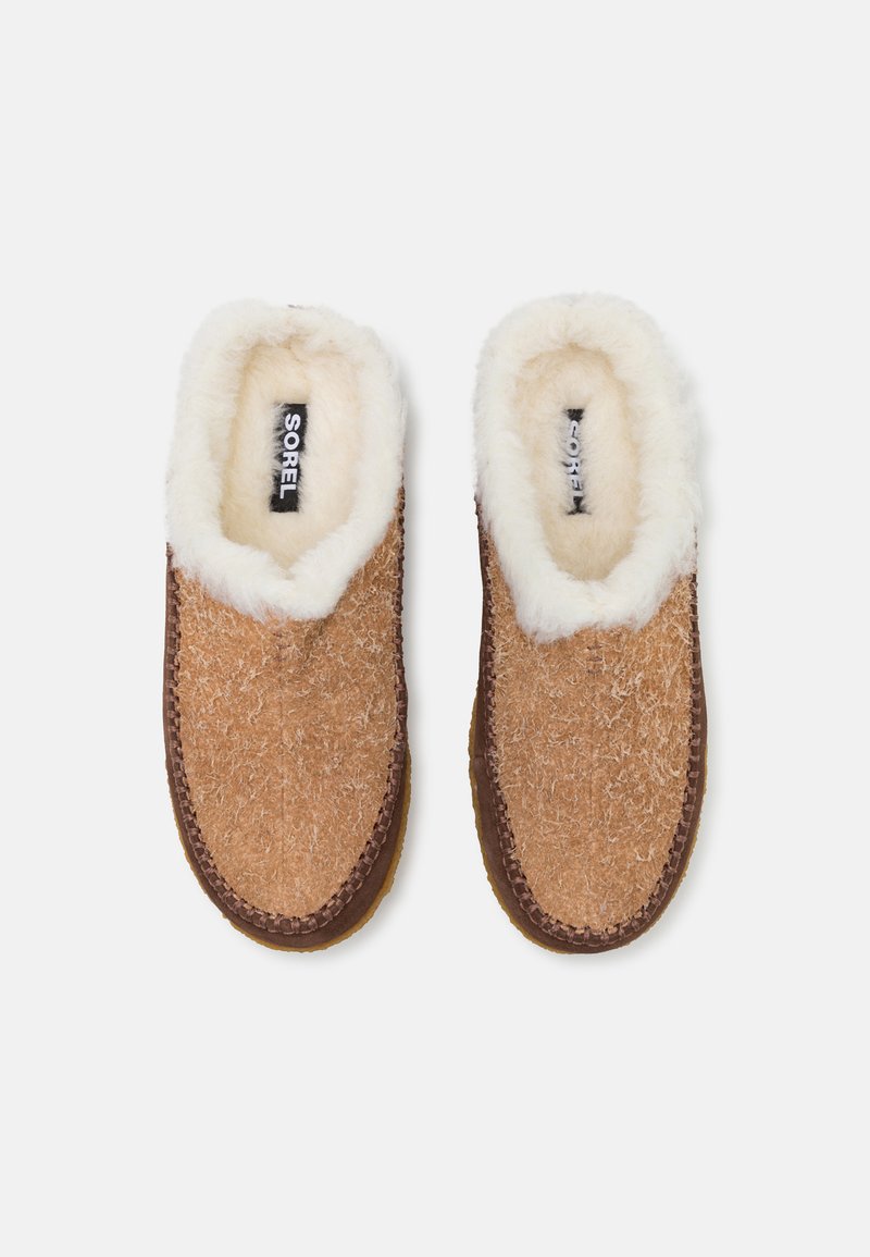 Bruine, zachte instapslippers met een pluizige witte voering, textuur aan de buitenkant en bruine stikseldetails. De zool is lichtbruin.