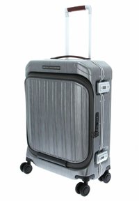 Valigia rigida grigia con scanalature verticali, manico retrattile, quattro ruote, serratura a combinazione e impugnatura marrone sulla parte superiore.