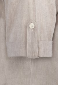 Beige linned skjorteærme med knaplukning. Har et struktureret væv og et spidst ærmedesign, der fremhæver en glat stoffinish.