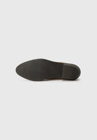 Suela de zapato de cuero marrón con una superficie de agarre de goma texturizada. El tacón tiene forma de bloque y es suave, con un diseño de borde plano.