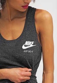 Mörkgrå tanktop i ett texturerat, lättviktsmaterial. Har en vit Nike-logotyp och texten "JUST DO IT" på bröstet.