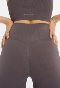 Donker mauve geribde legging met een hoge taille en naadloos ontwerp, met subtiele branding en accentstiksels op de tailleband.