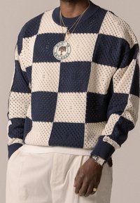Marineblauer und beigefarbener Strickpullover mit Schachbrettmuster, gerippten Bündchen und einem runden Logopatch. Strukturierter, atmungsaktiver Stoff.