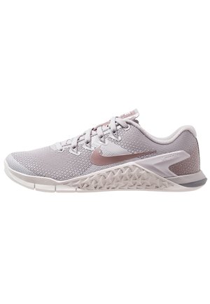 Chaussure d'entraînement Nike Metcon rose clair et gris avec dessus en maille texturée, lacets et semelle au motif géométrique, vue de profil.