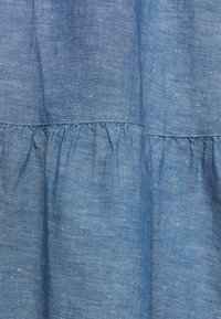 Tissu texturé bleu avec une couture horizontale froncée créant un effet volanté, montrant un gros plan des détails du matériau tissé.