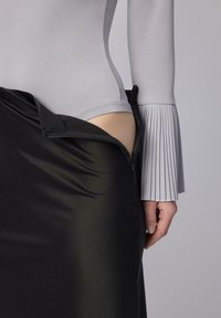 Body gri cu mâneci lungi plisate, purtat cu o fustă neagră din satin desfăcută parțial, expunând o secțiune a body-ului.