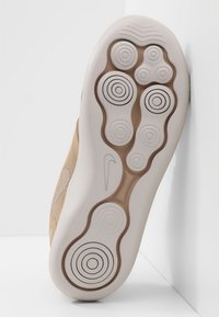 Nike-sneakersula med en beige gummibas utrustad med cirkulära mönster och spår, framhävd av en vit mellansula och logodetalj.