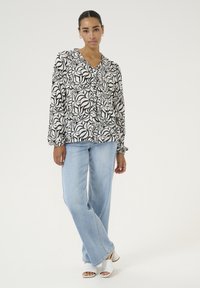 Black and white patterned blouse with a deep V-neck, long sleeves, and button closure, paired with light blue wide-leg jeans and white sandals.