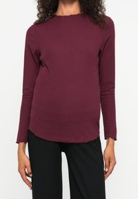 Burgundy ribbade långärmade topp med rund halsringning och vågig nederkant; matchad med svarta ribbade byxor. Tyget har en slät textur.