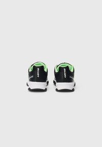 Schwarze und grüne Lotto-Sportschuhe von hinten gesehen, mit weißen Zwischensohlen und schwarzen Außensohlen auf einem schlichten weißen Hintergrund.