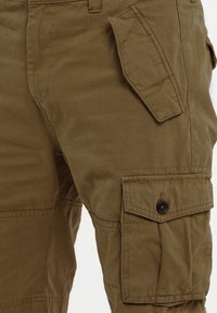 Olivenfarbene Cargo-Hosen aus Baumwolle mit glatter Textur, versehen mit mehreren Taschen, Knopf-Akzenten und verstärkten Nähten.