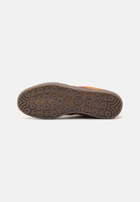 Semelle de chaussure avec un design en caoutchouc texturé, présentant des motifs circulaires et un logo proéminent, dans des tons de marron et d'orange.