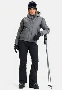 Grijze geïsoleerde skiparajka met capuchon, zwarte handschoenen en broek; uitgerust met skistokken en skibril, met een gestructureerd ontwerp.