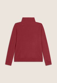Veste rouge à manches longues avec fermeture éclair et col haut, présentant une texture lisse et des détails de coutures le long du dos et des côtés.