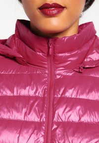 Magenta puchowa kurtka z wysokim kołnierzem i zapięciem na zamek, o błyszczącej, pikowanej fakturze i poziomym przeszyciu.