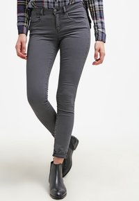 Jeans gris de corte ajustado hechos de tela elástica, con cinco bolsillos, trabillas para el cinturón y un dobladillo enrollado en el tobillo, combinados con botas negras hasta el tobillo.